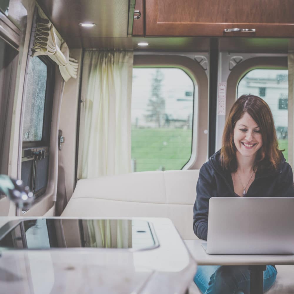 Young Woman Using a Laptop Inside a luxury Motorhome on a campground on a rainy day. Vintage look and grain added in post process.